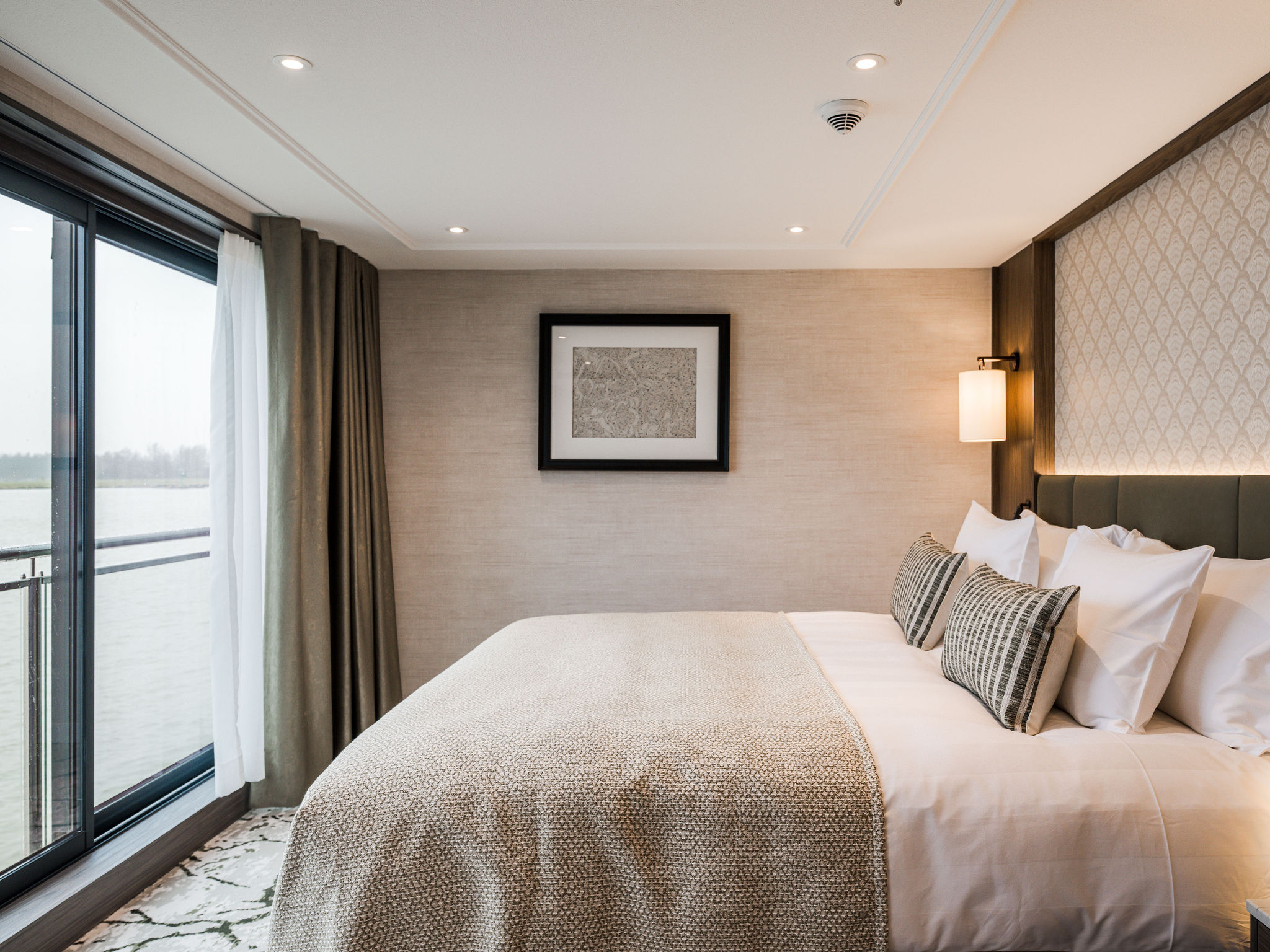 Bright cruise cabin with a king-sized bed, large panoramic window, soft neutral décor, and modern lighting.