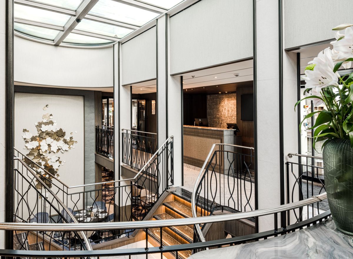 Elegant reception area with a central staircase, artistic wall installation, modern desk, and bright natural lighting.