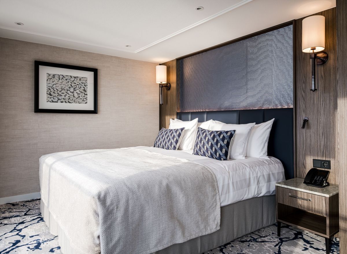 Luxurious river cruise cabin with a large double bed, elegant wall lamps, textured beige walls, and modern décor.