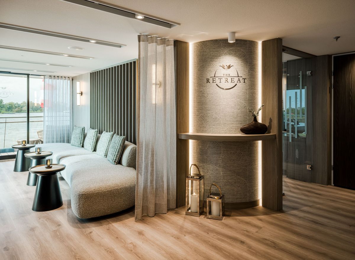 Modern onboard lounge with curved light-toned seating, floor-to-ceiling windows, soft lighting, and elegant wood accents.